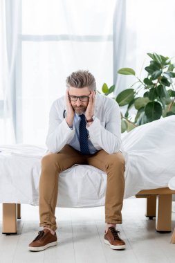 Beyaz önlüklü üzgün doktor yatakta oturup hastaneye bakıyor. 