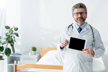 Beyaz önlüklü gülümseyen doktor elinde dijital tabletle hastanede fotokopi odası tutuyor. 