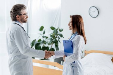 Beyaz önlüklü doktor ve gülümseyen meslektaşı hastanede el sıkışıyor. 