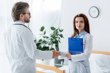 Beyaz önlüklü doktor ve meslektaşı hastanede el sıkışıyor. 