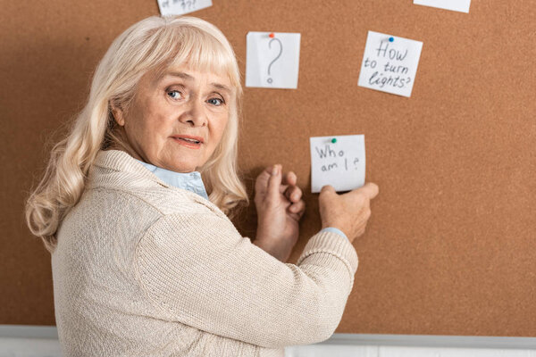 selective focus of senior woman with alzheimer disease touching paper with who am i letters 