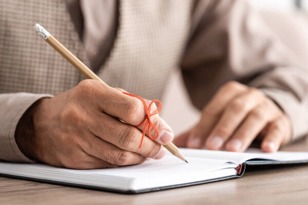 cropped view of retired man with alzheimers disease string human finger reminder writing in notebook 