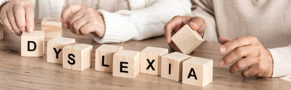 panoramic shot of senior woman sitting near sick husband and wooden cubes with dyslexia letters 