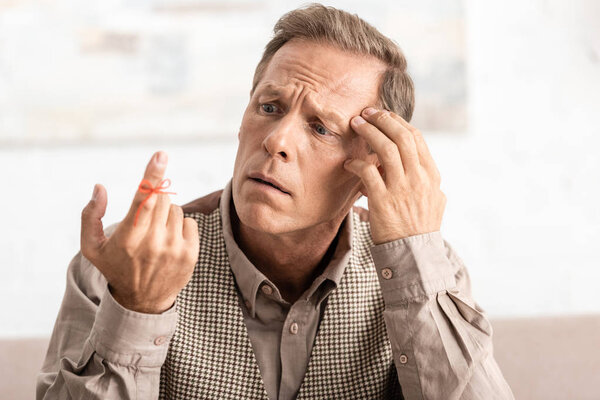 selective focus of confused retired man looking at alzheimers disease string human finger reminder 