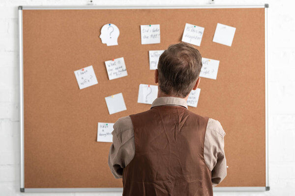 back view of sick senior man standing near board with papers 