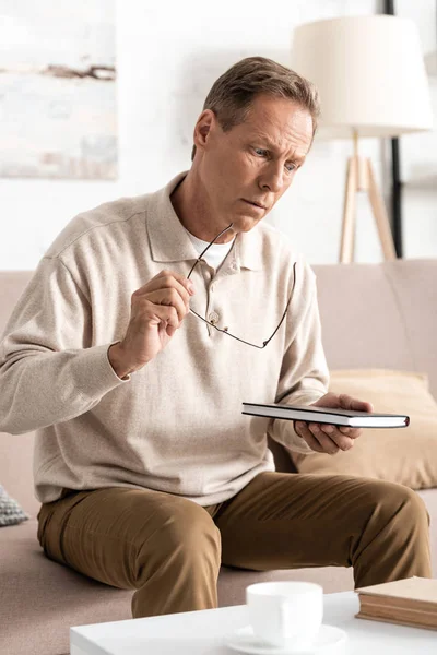 Ledsen Senior Man Sitter Soffan Och Håller Anteckningsbok — Stockfoto