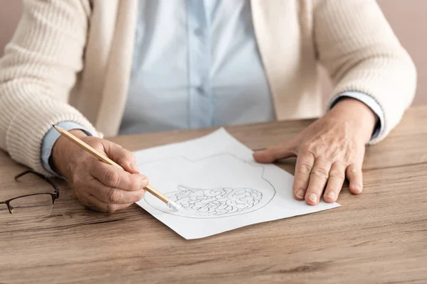 Vista Cortada Mulher Aposentada Segurando Papel Com Desenho Mesa — Fotografia de Stock