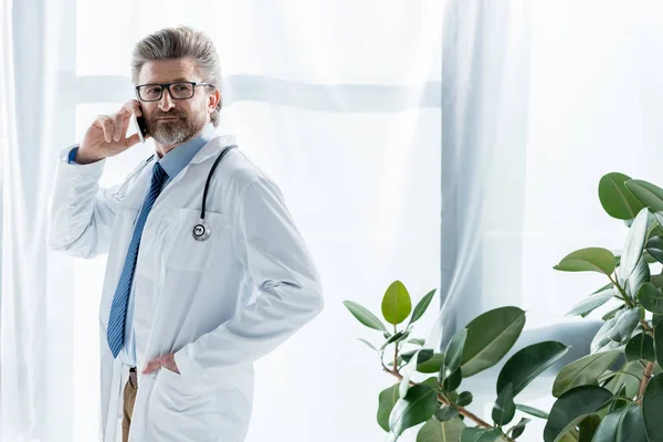 Όμορφος Γιατρός Λευκό Παλτό Χέρι Στην Τσέπη Μιλώντας Στο Smartphone — Φωτογραφία Αρχείου