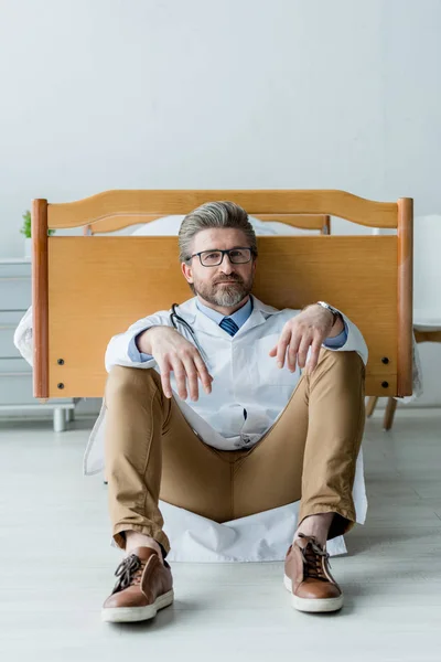 Guapo Médico Bata Blanca Sentado Suelo Mirando Cámara Hospital — Foto de Stock