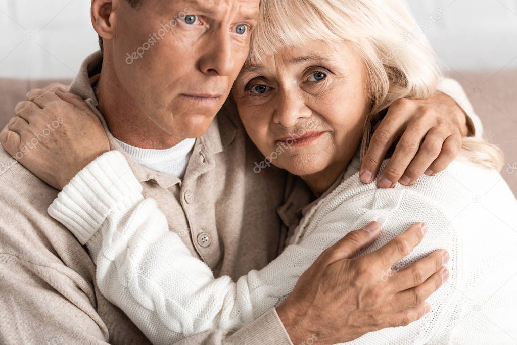 upset senior woman hugging with sick husband at home 