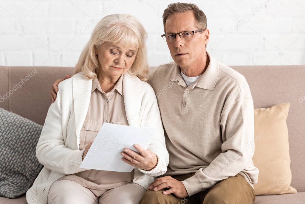 retired man in glasses sitting near sick wife with alzheimer holding paper 