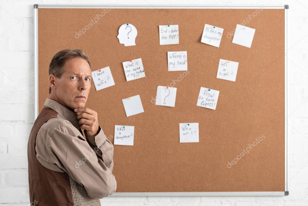 pensive retired man standing near papers with letters on bard 