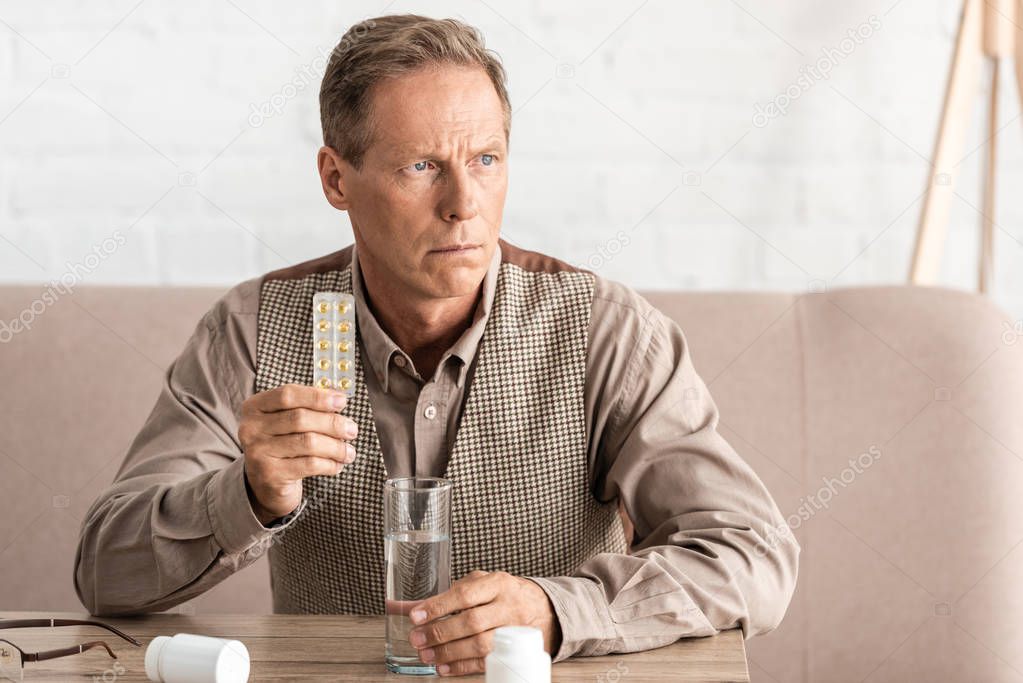 sick senior man with alzheimer holding glass of water and pills 