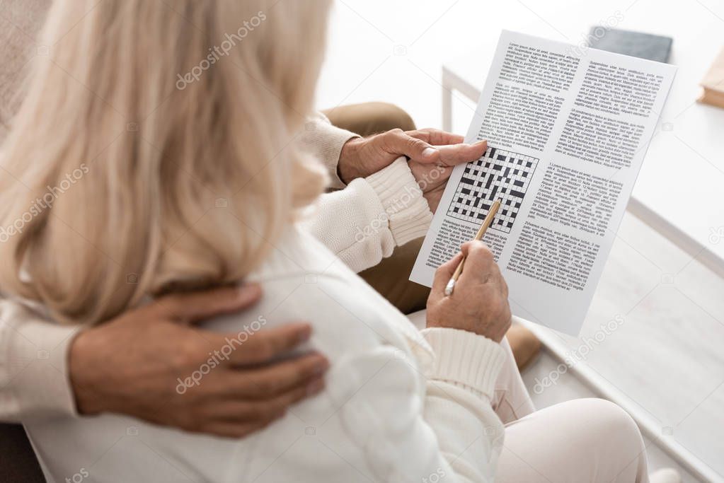 cropped view of senior man hugging wife with pencil and crossword 