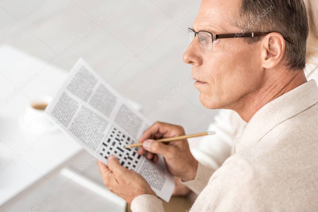 selective focus of senior man in glasses holding pencil near crossword in newspaper 