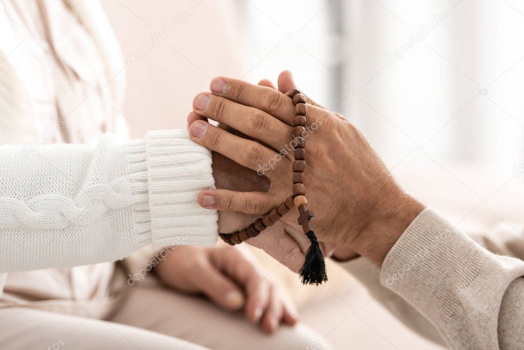 cropped view of senior man with rosary breads holding hands with wife