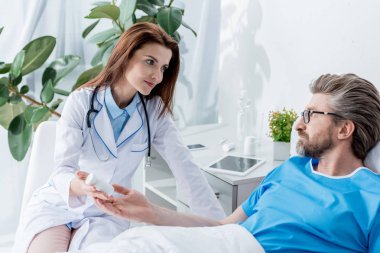 Beyaz önlüklü doktor hastanede yatan hastaya ilaç şişesi veriyor. 