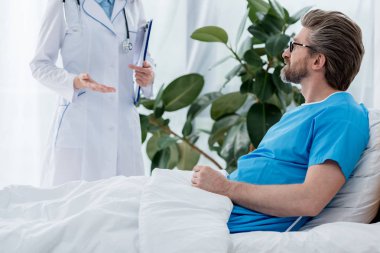 Beyaz önlüklü doktorun hastanedeki hastayla konuşma görüntüsü. 