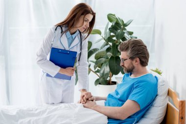 Hastanedeki üzgün hastanın elini tutan beyaz önlüklü doktor. 
