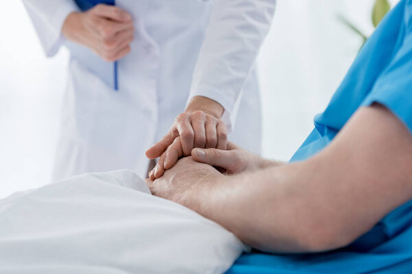 обрезанный вид врача в белом халате, держащего пациента за руку в больнице
 