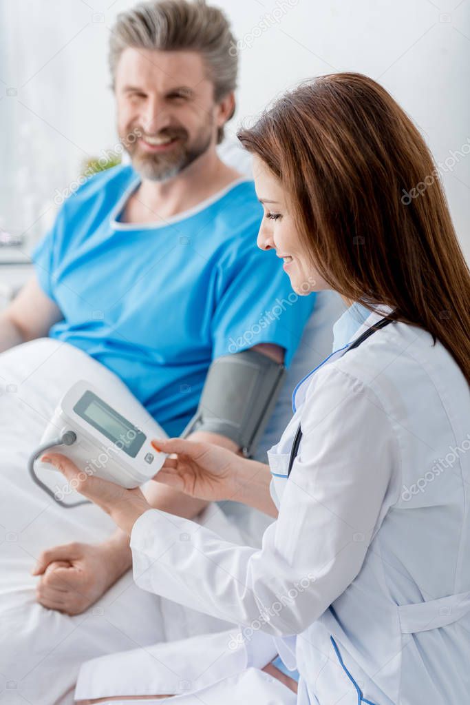 smiling doctor in white coat measuring blood pressure of patient in hospital 