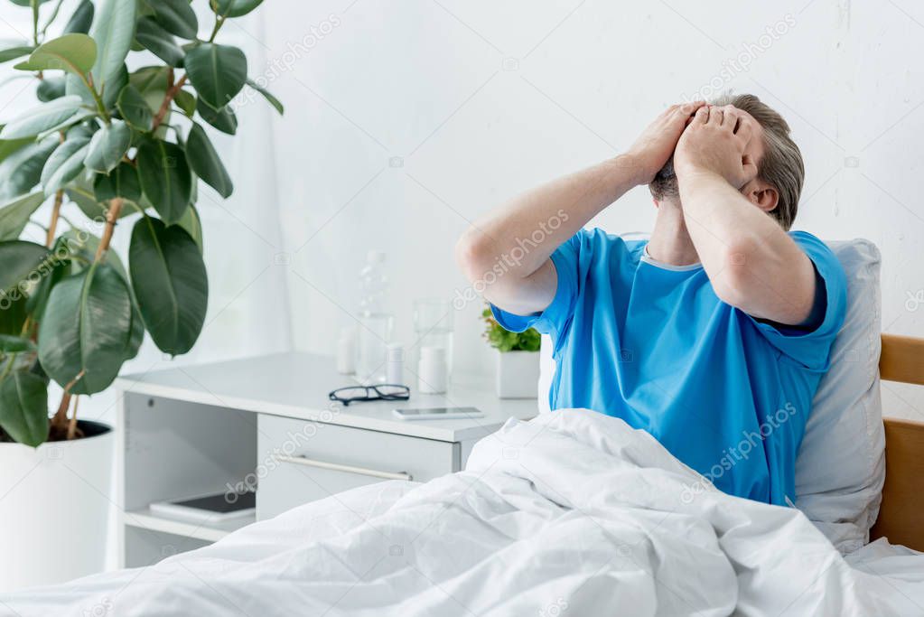 sad patient in medical gown sitting on bed and crying in hospital 