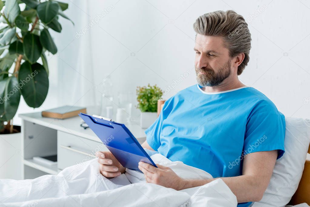 patient in medical gown looking at clipboard in hospital 