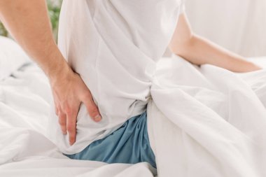 Kırpılmış insan görüntüsü beyaz bir yatakta oturuyor ve fileto ağrılarından muzdarip