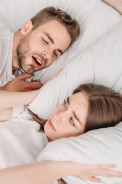 Uyanmış bir kadın, yatakta horlayan bir kocanın yanında, yastıkla kulaklarını tıkamış.
