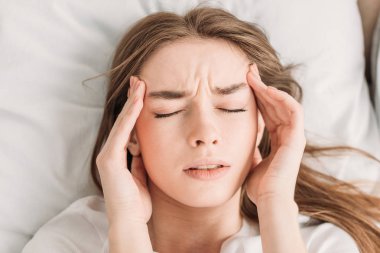 top view of young woman with closed eyes touching head while suffering from migraine clipart