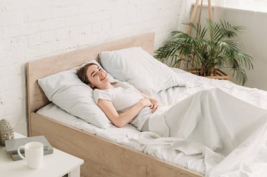 Neşeli kız yatakta yatarken kameraya bakıyor, gülüyor ve el ele tutuşuyor.