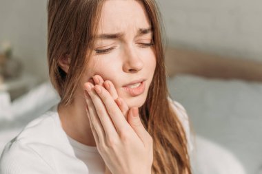 Genç bir kadın diş ağrısı çekerken yanağa dokunuyor.