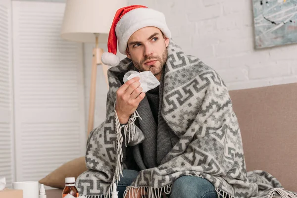 サンタ ハットの男は毛布に包まれてナプキンを手にしながら — ストック写真