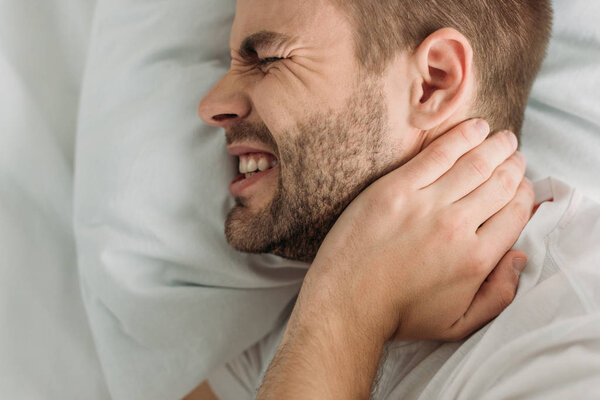 Top view of young man touching neck while suffering from pain
 