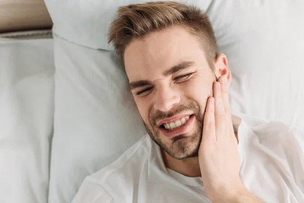 歯痛に苦しみながら頬に触れる若い男のトップビュー — ストック写真