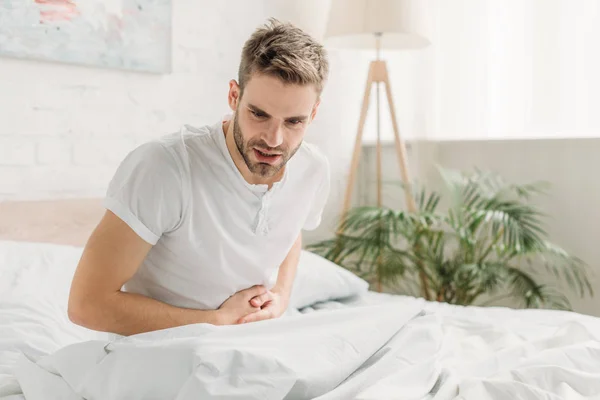 Joven Sentado Sobre Ropa Cama Blanca Sufriendo Dolor Estómago — Foto de Stock