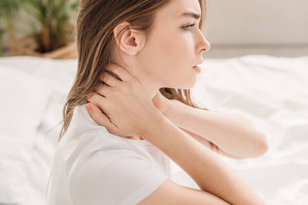 sad girl looking away while sitting in bed and suffering from neck pain