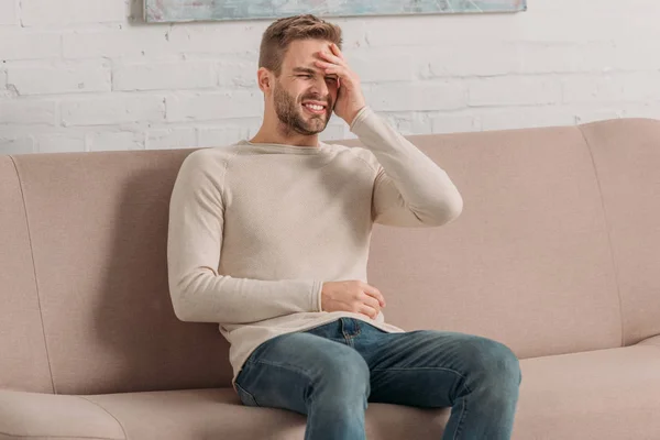 Hombre Fruncido Sentado Sofá Con Los Ojos Cerrados Mientras Sufre — Foto de Stock