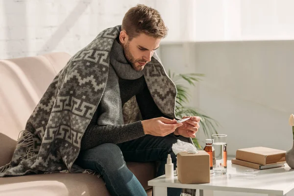 Uomo Malato Avvolto Una Coperta Seduto Sul Divano Guardando Termometro — Foto Stock