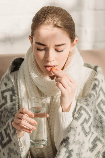 病気の少女は毛布に包まれ水を飲みながら薬を飲み — ストック写真