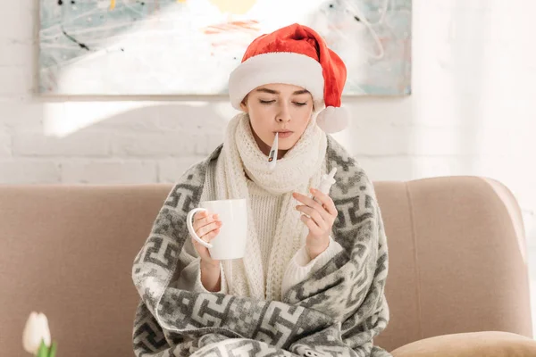 Krankes Mädchen Weihnachtsmannmütze Misst Temperatur Während Nasenspray Und Eine Tasse — Stockfoto