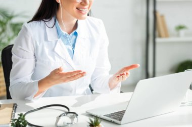 Gülümseyen doktorun klinikteki laptopta hastayla çevrimiçi istişare yaptığı görüntüler.