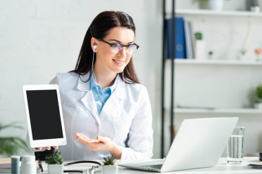 Bilgisayarda online danışmanlık yaparken dijital tablette teşhis koyan gülümseyen doktor 