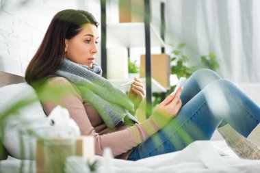 Termometresi olan hasta bir kadın akıllı telefondan doktorla çevrimiçi istişare yapıyor.