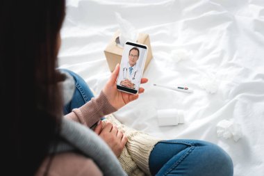 Haplı ve termometresi olan hasta bir kadının akıllı telefondaki erkek doktorla online istişare yaptığı görüntüler.