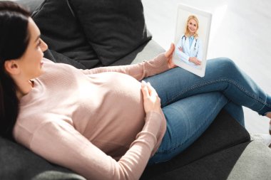 Çekici hamile kadın dijital tablette kadın doktorla çevrimiçi danışmanlık yapıyor. 