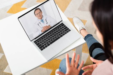 Kırık bacaklı bir kadının dizüstü bilgisayarında doktorla görüşmesi. 