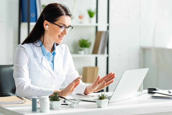attractive smiling doctor having online consultation with patient on laptop in clinic office
