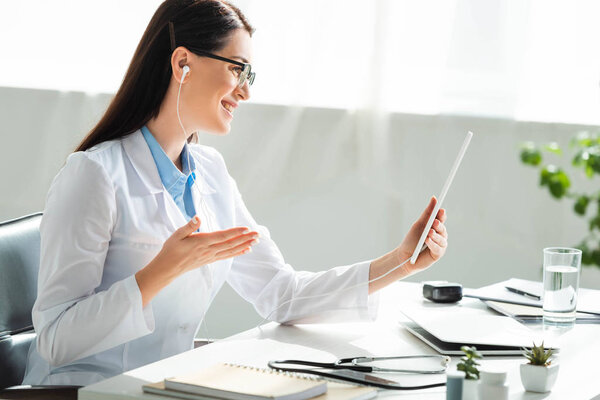 smiling doctor having online consultation on digital tablet in clinic office with laptop