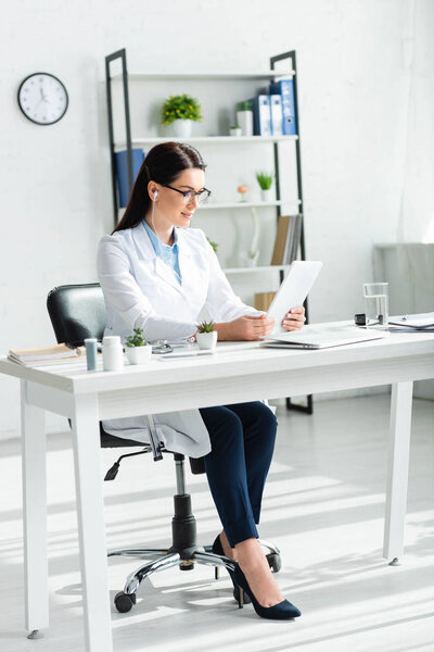 beautiful doctor having online consultation on digital tablet in clinic office with laptop